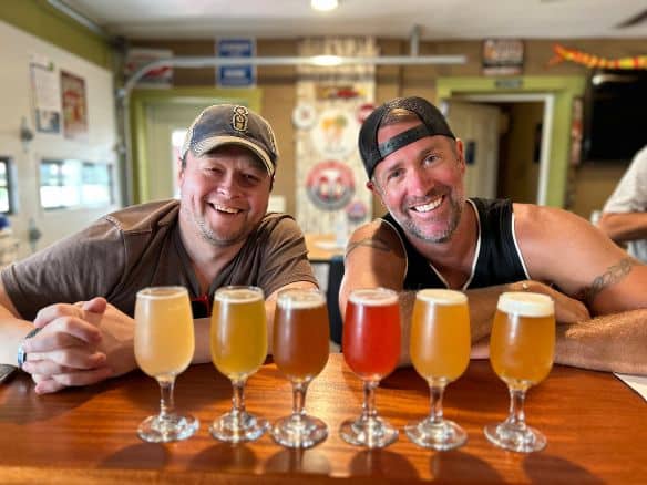 Two men with full beer glasses in line in front of them