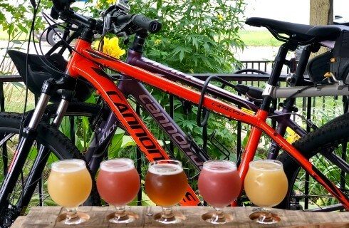 Two bicycles by a black railing next to a flight of different colors of beer