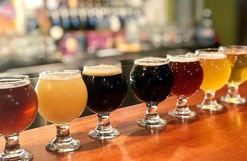 Wood bar countertop with seven glasses of different colors of beer