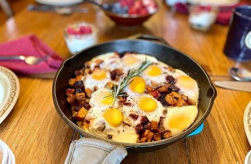 Dining table with egg and potato breakfast dish in a cast iron pan with a bowl of berries