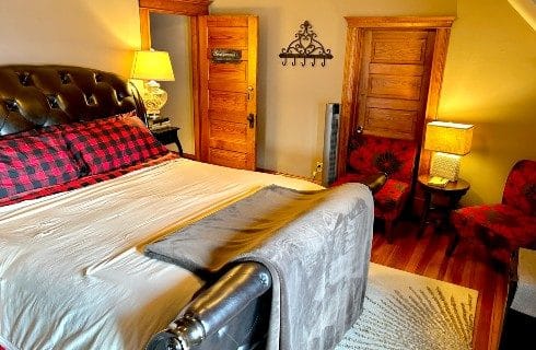 Cozy bedroom featuring king bed with black leather headboard and footboard and two red and black sitting chairs