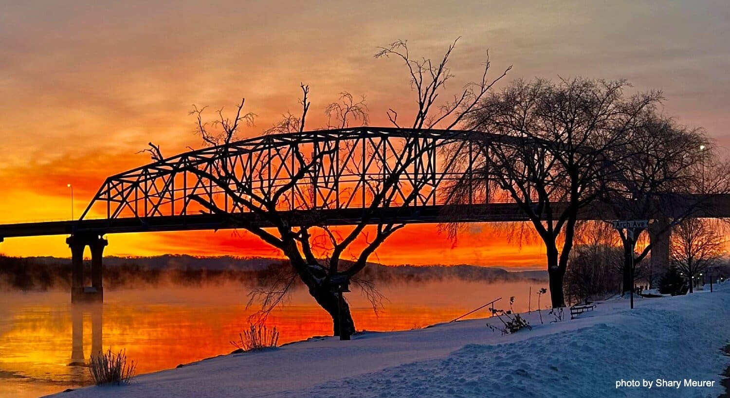 Large bridge over a river of water at sunset with orange and red skies