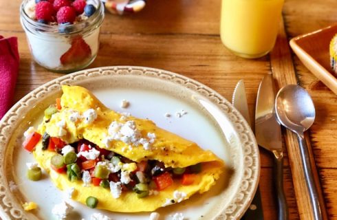 Dining table with white round plate holding an omelette, jar of yogurt with berries, a muffin and glass or orange juice