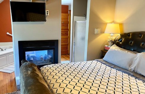 Bedroom with king bed, gas fireplace that is seen from both sides of the room and corner tub