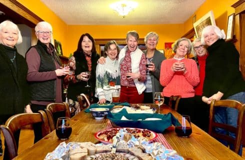 A group of nine ladies gathered around a dining room table in a home