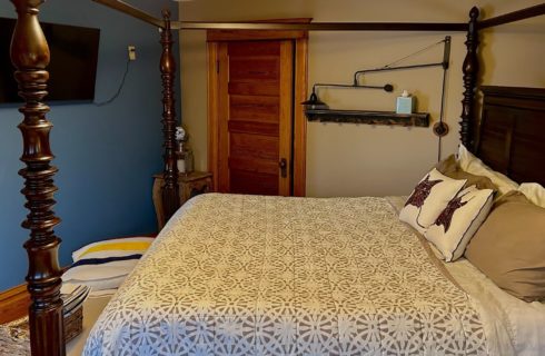 Bedroom with four-poster king bed with white and taupe quilt and TV on a blue wall