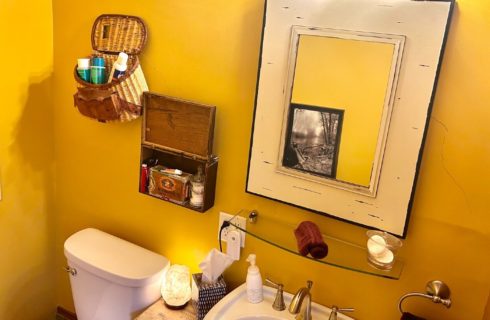 Bathroom with yellow walls, pedestal sink, toilet and large white framed mirror