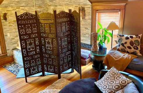 Bathroom with corner jacuzzi tub behind a privacy screen, bench, club chair and two windows