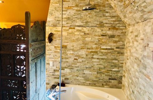 Corner jacuzzi tub with stone wall feature, silver shower head and a privacy screen