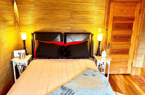 Bedroom with natural grass wallpaper, queen bbed and two white side tables with lamps