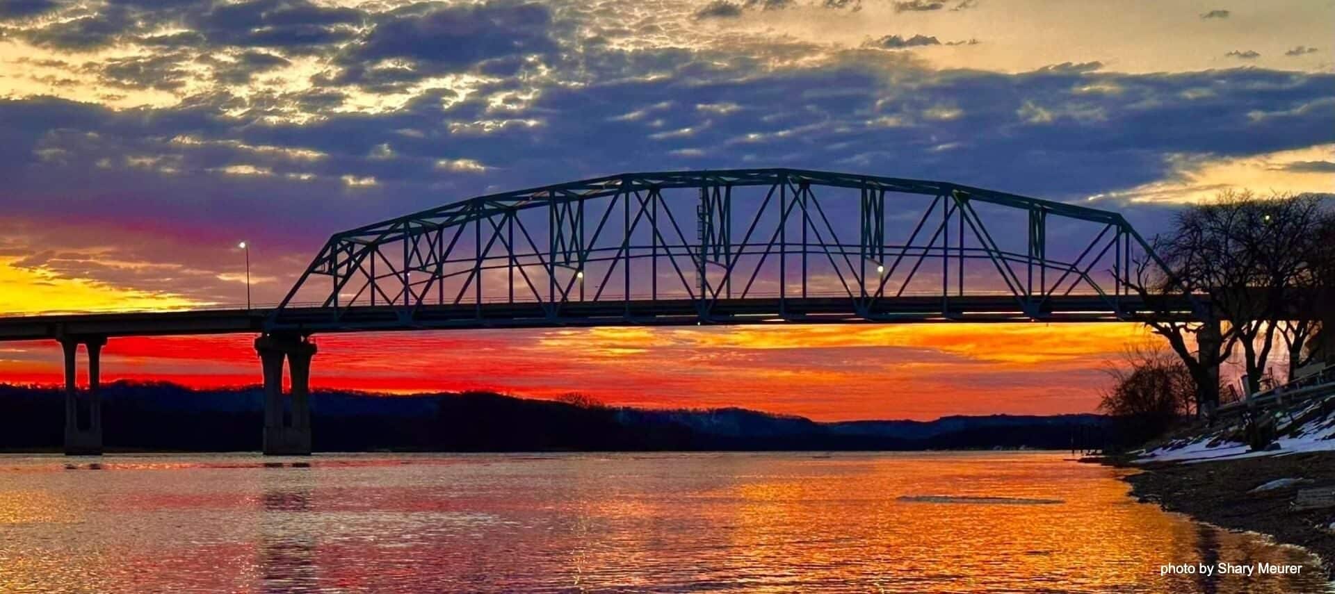 Large bridge over a river of water at sunset with orange and red skies