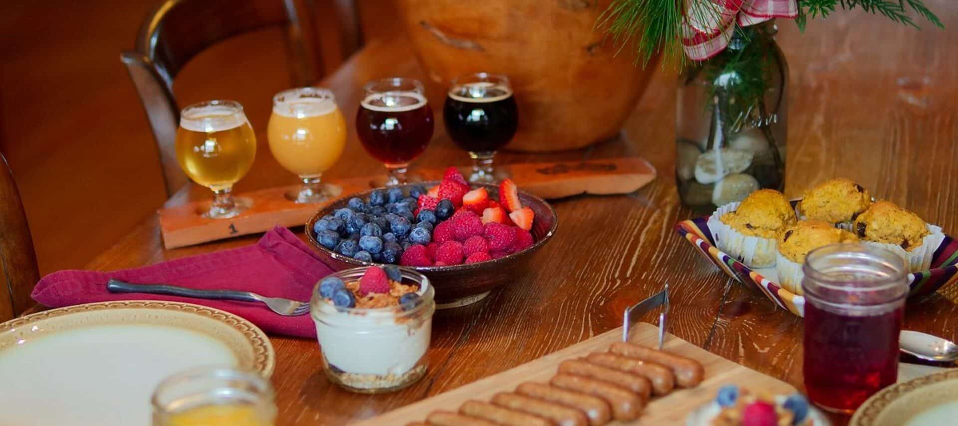 Dark wood dining table with flight of juice glasses, bowl of berries, muffins and platter of sausage links