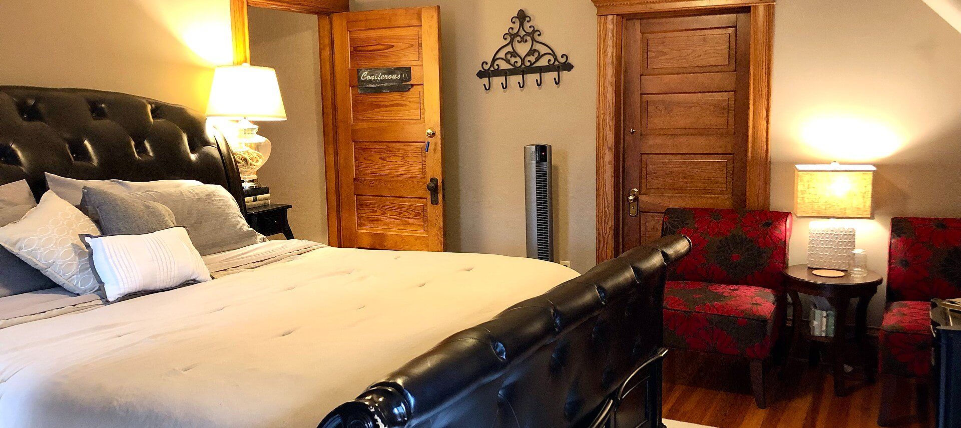 Cozy bedroom featuring king bed with black leather headboard and footboard and two red and black sitting chairs