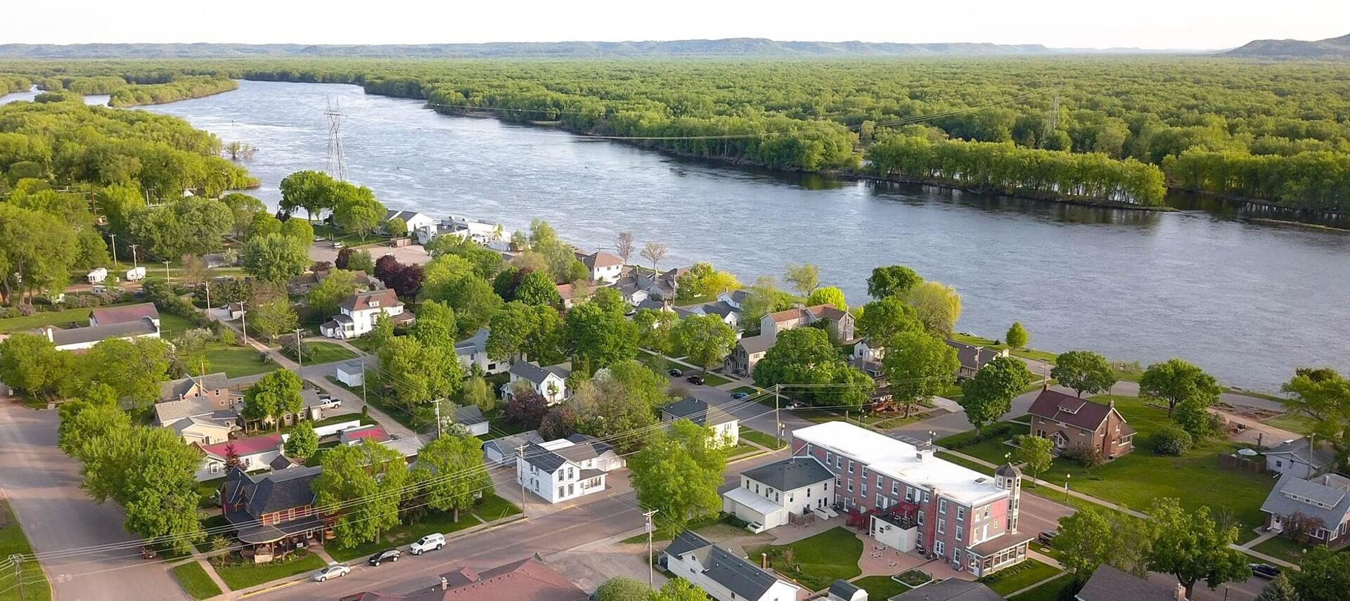 Overhead drone image showing homes near a large river surrounded by trees