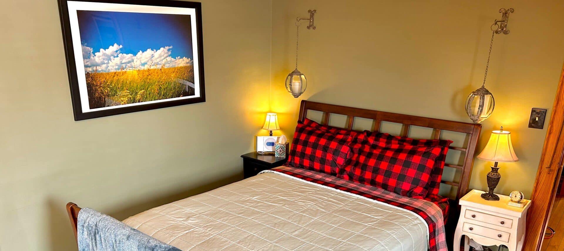 Bedroom with queen bed with black and red buffalo check sheets and pillows, and two side tables with lamps