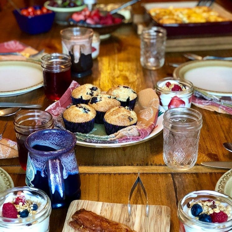 Wood dining ready for breakfast with plates, muffins, bowls of berries, cups of yogurt, platter of bacon