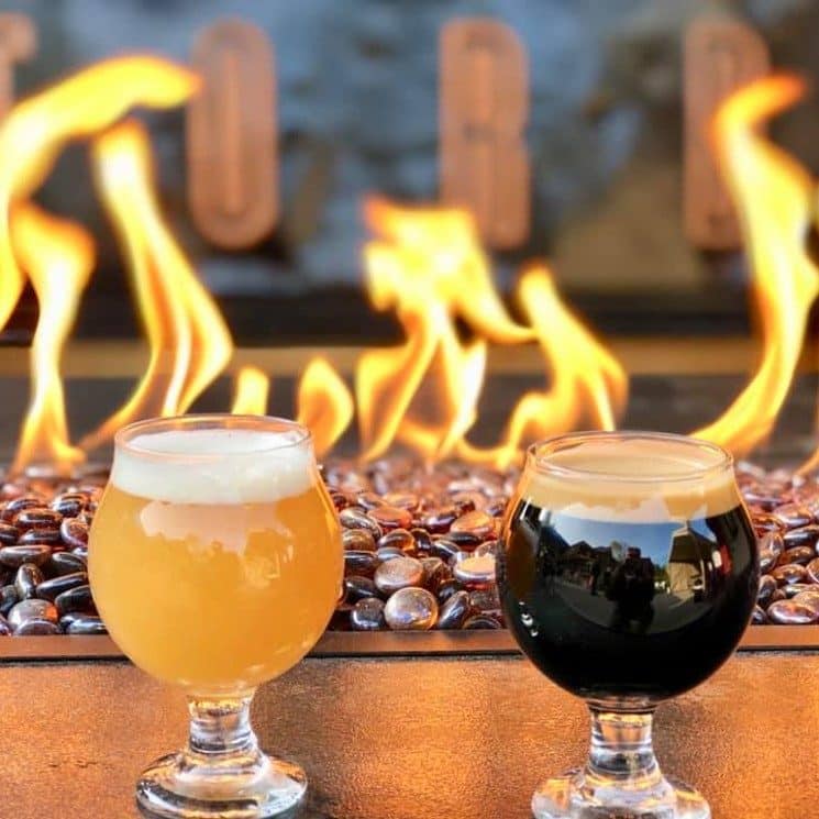 Two glasses of beer, one dark and one light, by a fire on stones