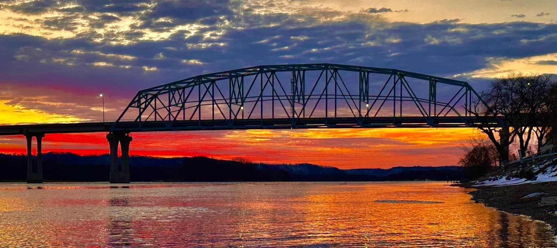 Large bridge over a river of water at sunset with orange and red skies