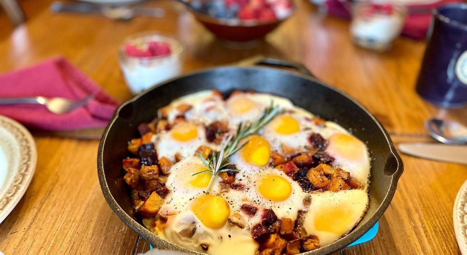Dining table with egg and potato breakfast dish in a cast iron pan with a bowl of berries