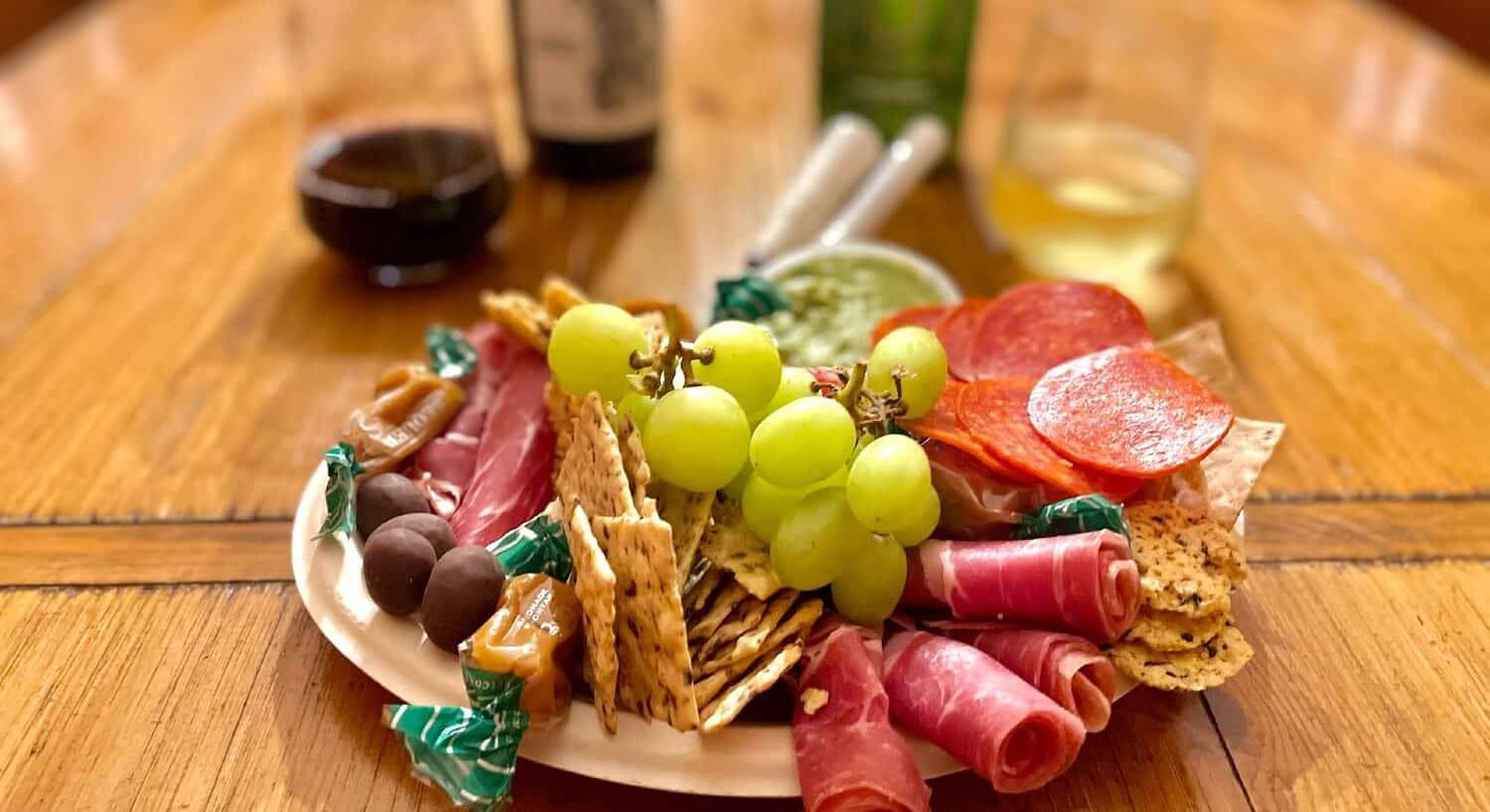 Charcuterie platter with fruit, meats, crackers and chocolates with two glasses of wine