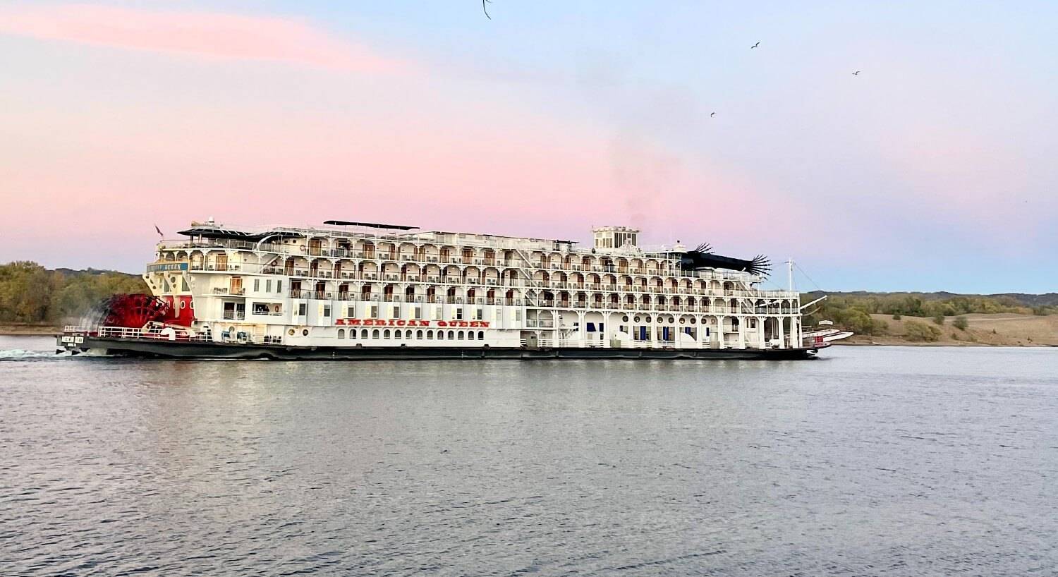 Large red and white paddlewheel boat cruising down a river